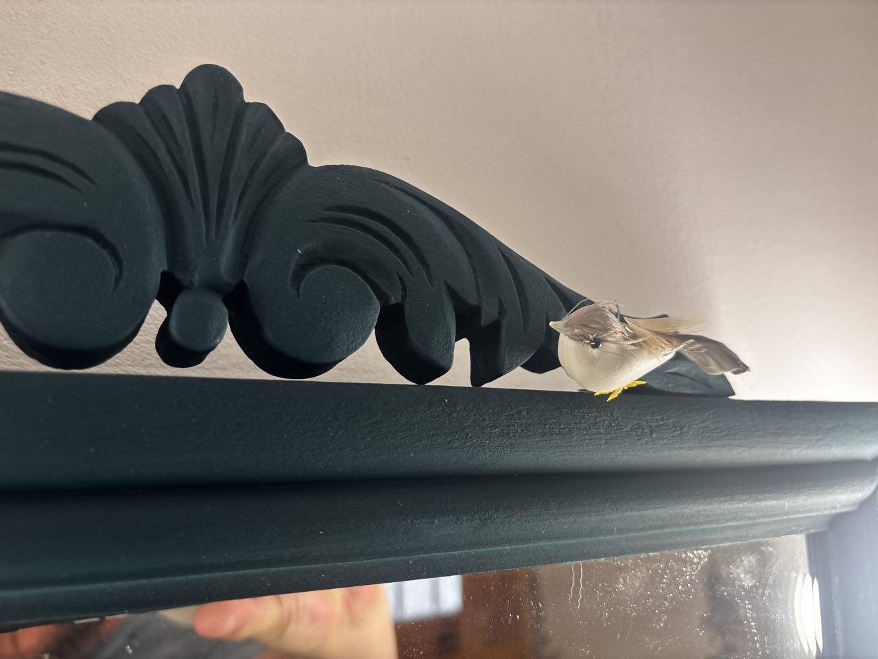 Pájaro decorativo posado en el marco tallado de un espejo